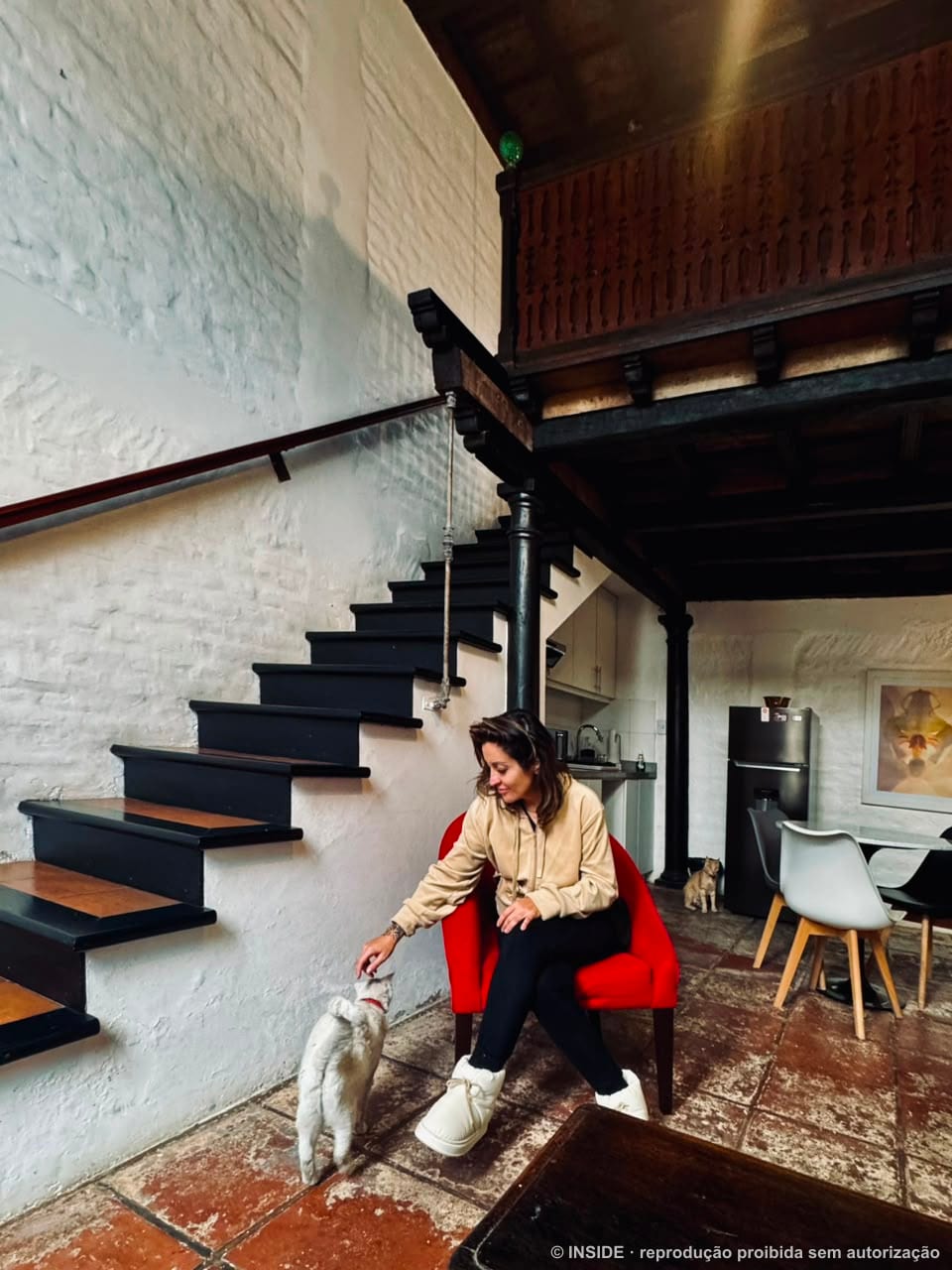Sara Rollemberg sentada na escada de um loft com um gato, bastidores INSIDE